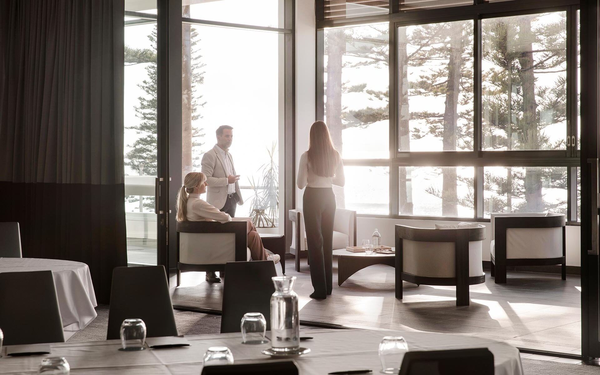 Business guests gathered in an event room at Elysium Manly overlooking pine trees, showcasing Manly event spaces