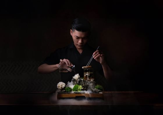Bartender elegantly pouring liquid into a glass atop a rocky display in 2 Lam Son at Park Hyatt Saigon