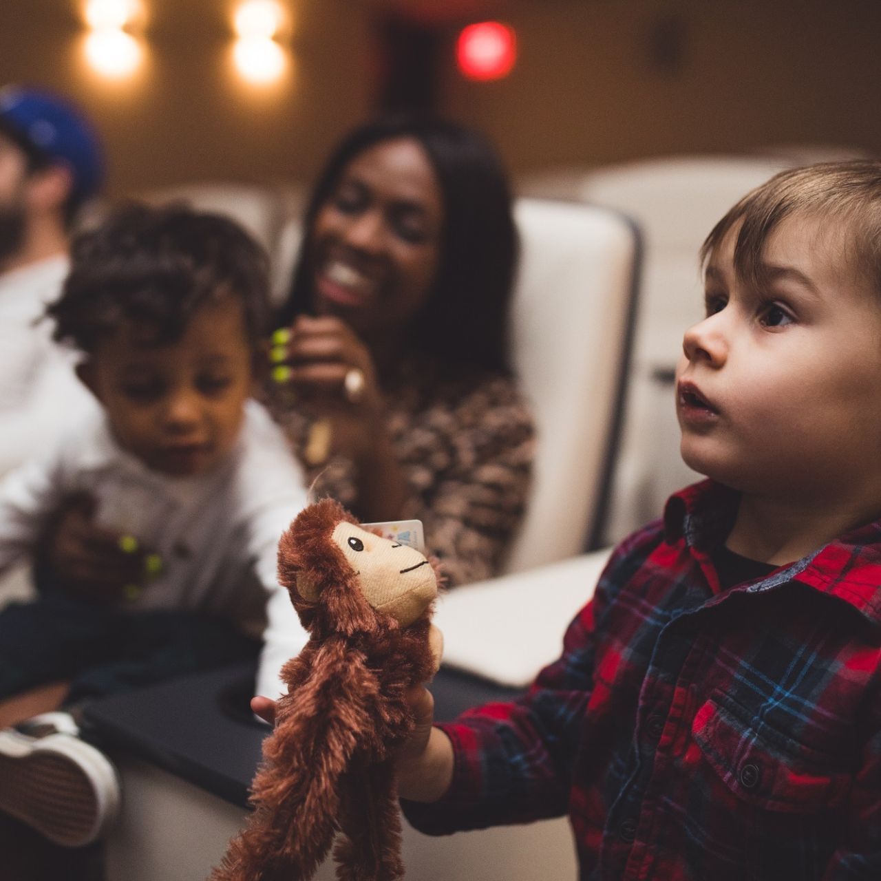 Young child holding a plush monkey while watching a movie with family in comfortable cinema seating at Hotel X Toronto