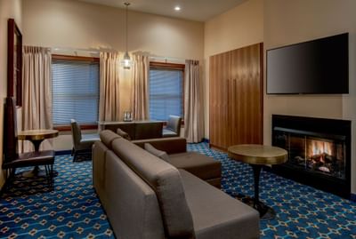 Suite living area featuring a dining table with a couch & television above a fireplace near windows at Harborside Inn Boston