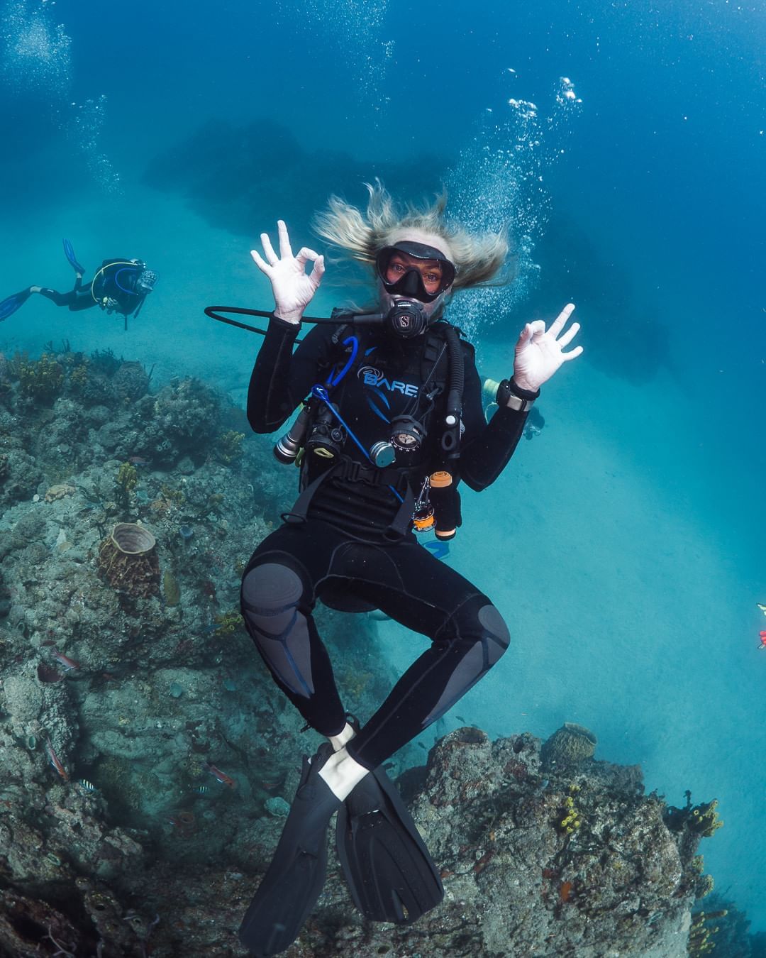 Scuba diver poses underwater, making a hand sign, surrounded by vibrant coral near Golden Rock Resort