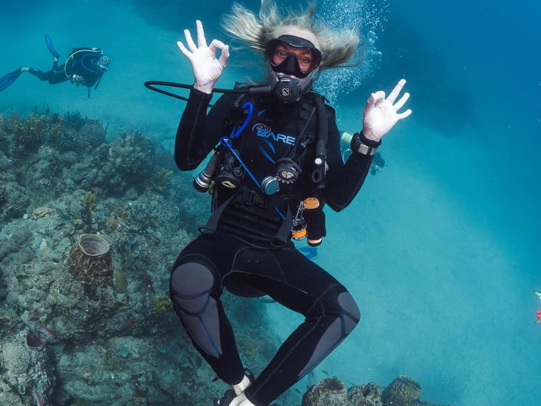 Scuba diver poses underwater, making a hand sign, surrounded by vibrant coral near Golden Rock Resort