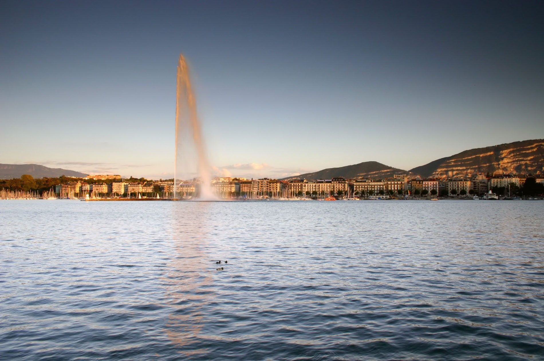 Tall water fountain Jet d'Eau spraying into the sky by the city skyline near Warwick Geneva