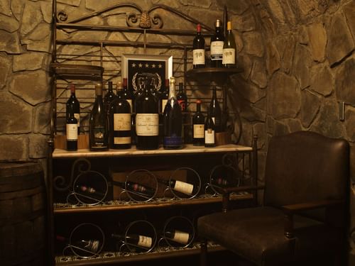 Cozy wine cellar with stone walls, a leather chair, and bottles of wine at La Cava de Santiago in Hacienda del Mar Los Cabos.