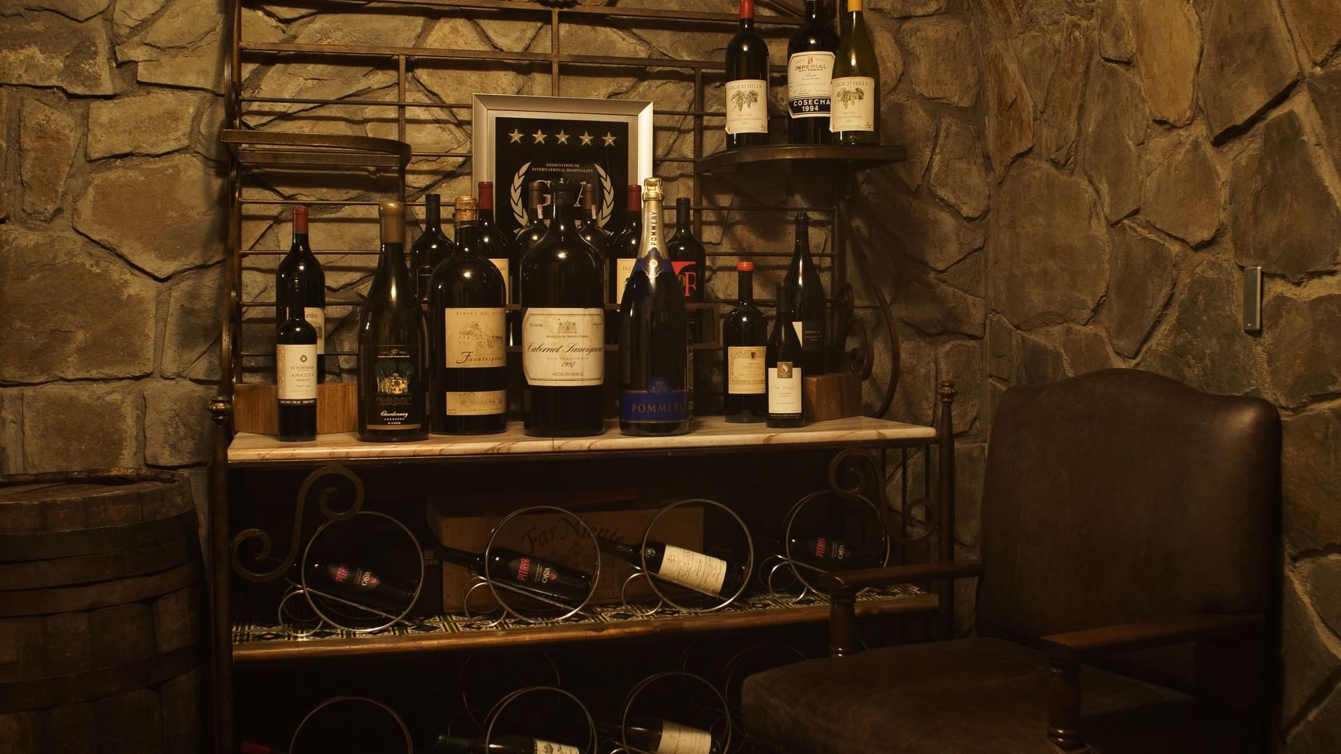 Cozy wine cellar with stone walls, a leather chair, and bottles of wine at La Cava de Santiago in Hacienda del Mar Los Cabos.