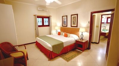 King bed with green runner between glowing lamps and beside a woven armchair in a room at Sugar Cane Club Hotel & Spa
