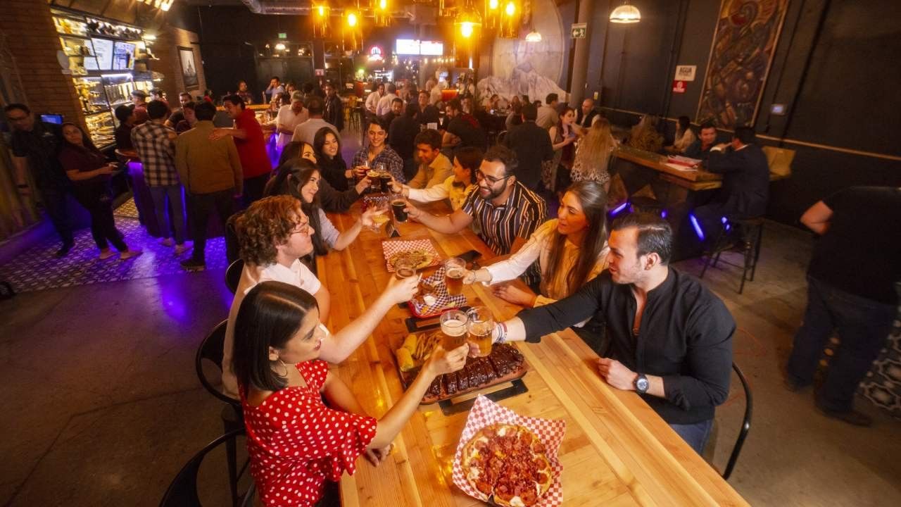 Group of friends toasting with beer over a large table of pizza and ribs at Camino Real Pedregal Mexico
