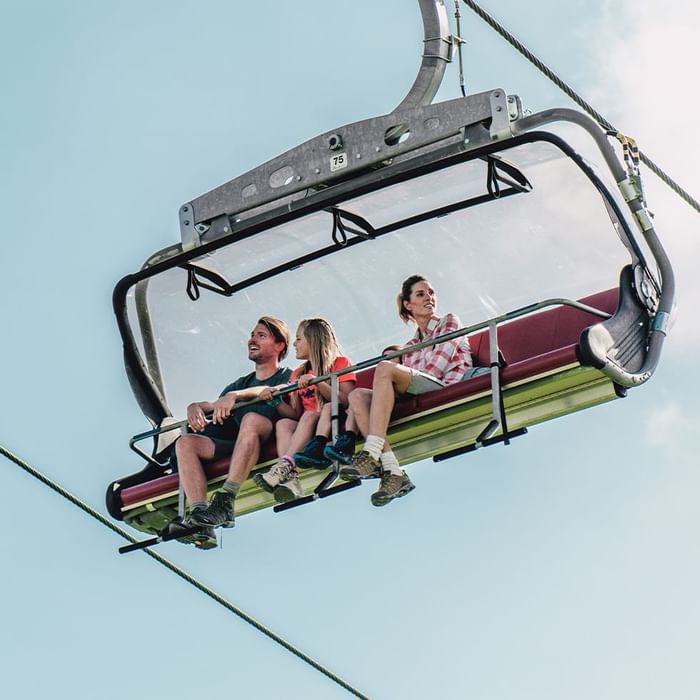 Three people on a ski lift, smiling, under a clear blue sky with clouds.