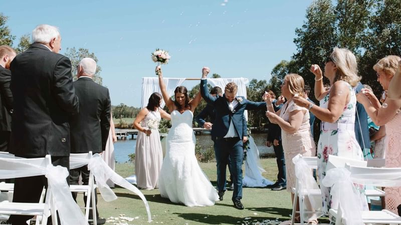 Wedding couple walking down the aisle with a lake in the backdrop at Mercure Kooindah Waters