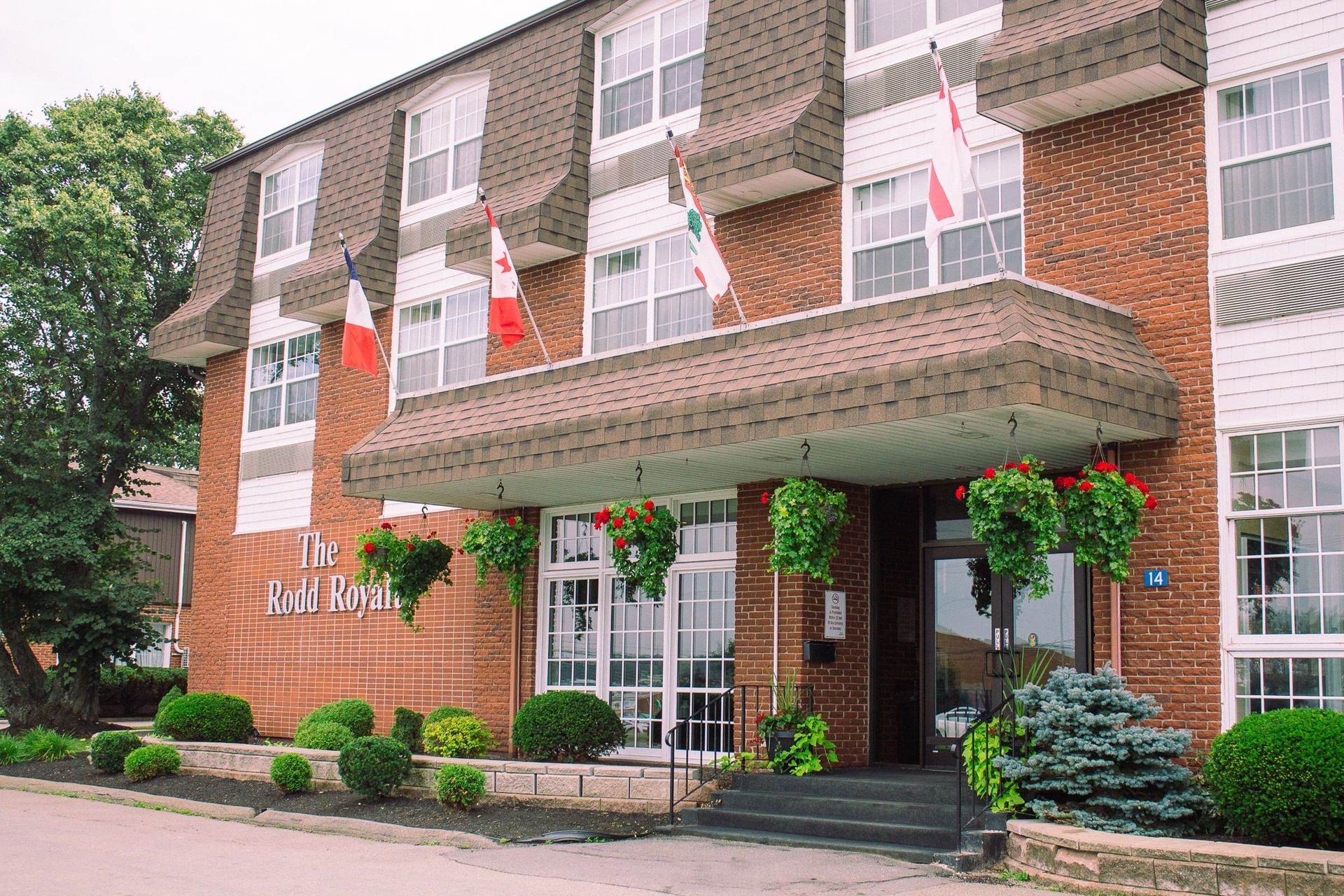 Red brick hotel exterior with flags and hanging flower baskets under a brown shingled awning at Rodd Royalty
