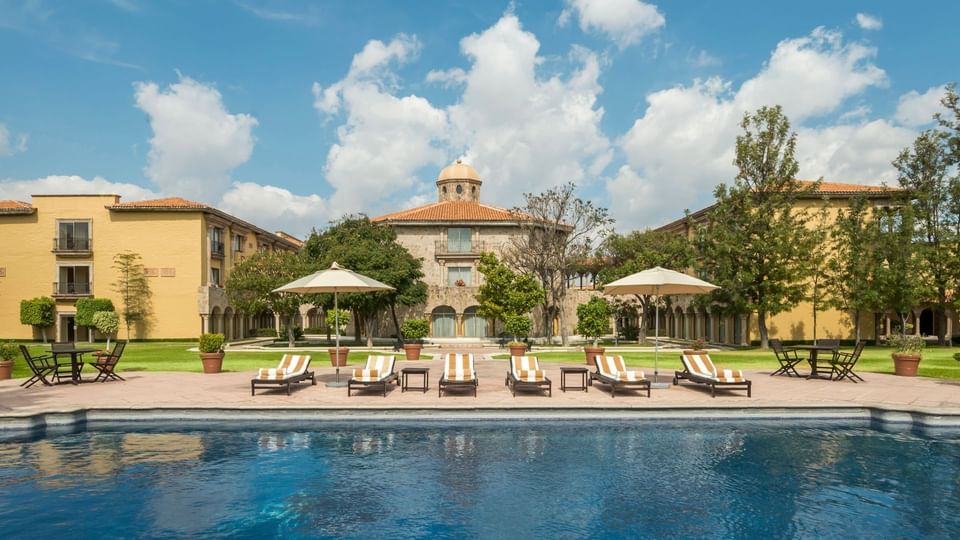 Serene outdoor pool with striped loungers and colonial architecture behind at Quinta Real Aguascalientes