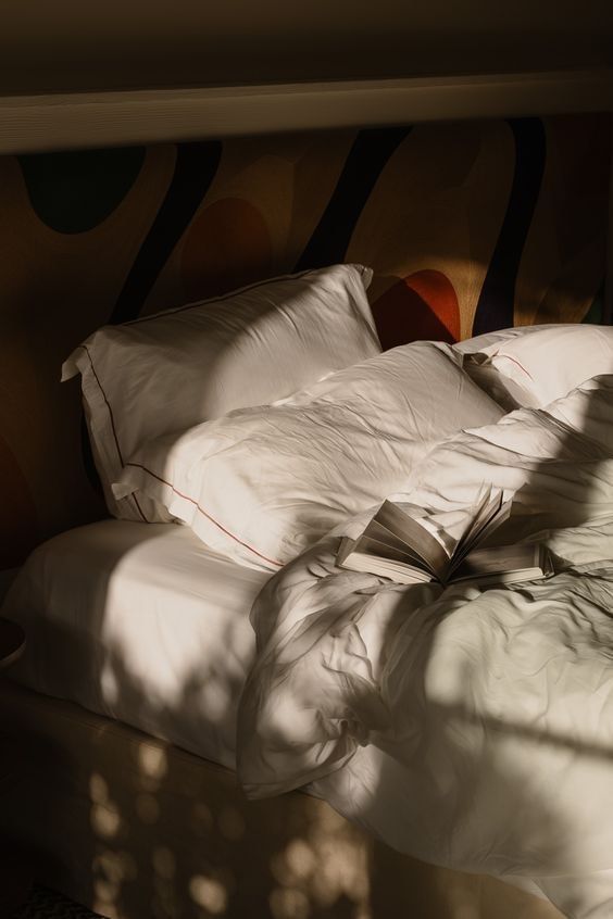 A close-up of a bed with white bedding, pillows, and an open book on top.
