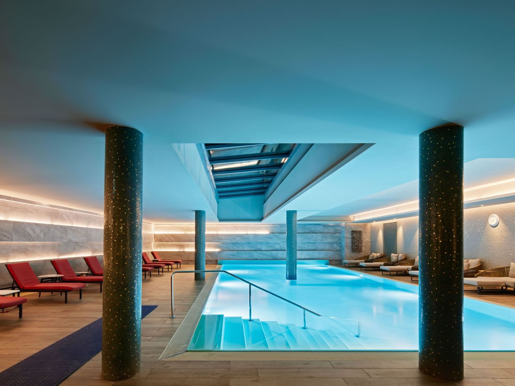 Elegantes Schwimmbad mit blauem Wasser, roten Liegen und gemusterten Säulen – Titanic Chaussee Berlin.