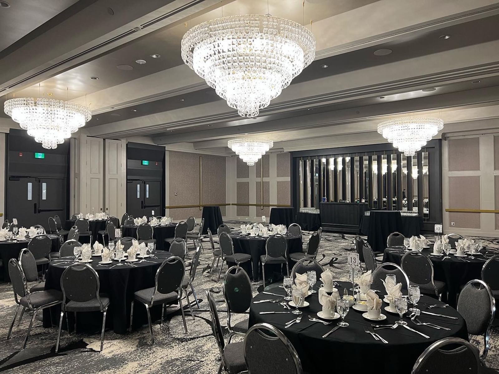 Carriage House large hall with round tables set for a formal dinner under chandeliers, chairs around tables.