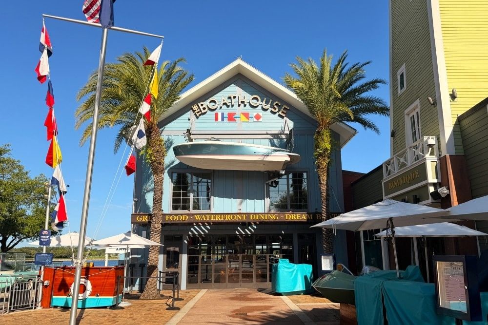 The front of The Boathouse restaurant at Disney Springs, decorated with maritime flags and a large speedboat hanging over the main sign. 