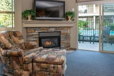 Patterned chair next to a stone fireplace, patio doors open to the pool deck in Hilltop Suite at Hilltop Inn, Salmon Arm