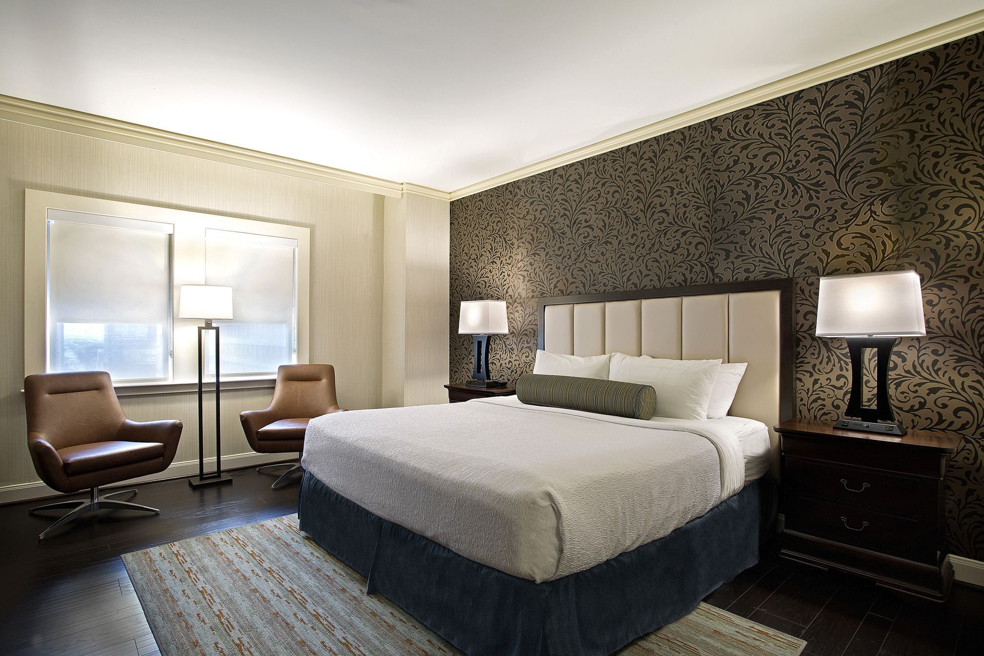 A hotel room with a large bed, two nightstands, a sitting area with two chairs, and a window.