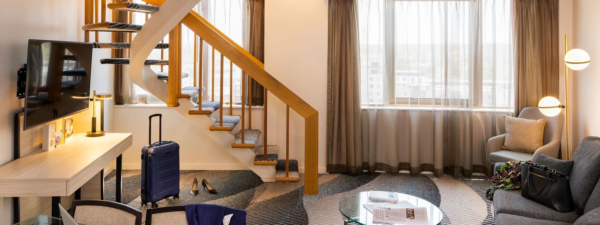TV lounge by the window in the King Spa Suite at Novotel Sydney Parramatta, featuring carpeted floors beneath the stairs