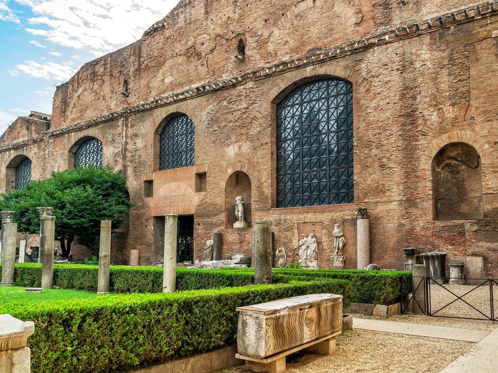 Historic brick wall with arched windows at the Baths of Diocletian, surrounded by lush greenery near The Guardian Hotel