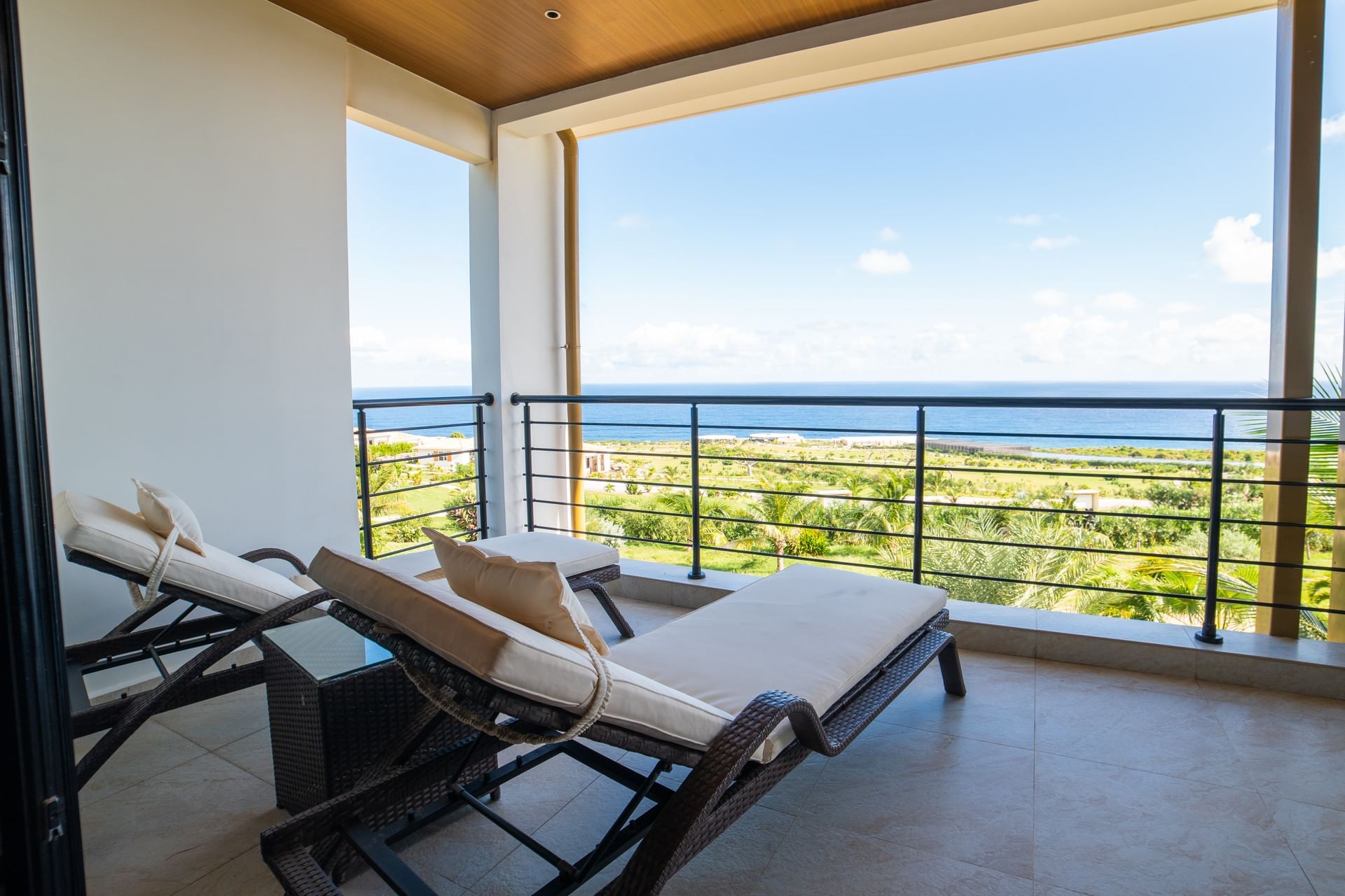 Balkon met twee ligstoelen met uitzicht op weelderig groen en de oceaan in Deluxe Ocean View Room bij Golden Rock Resort