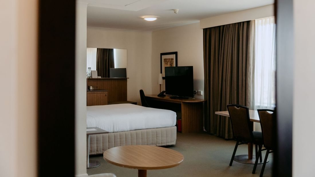 Hotel room with bed, desk, TV, chair, table, and window with curtains.