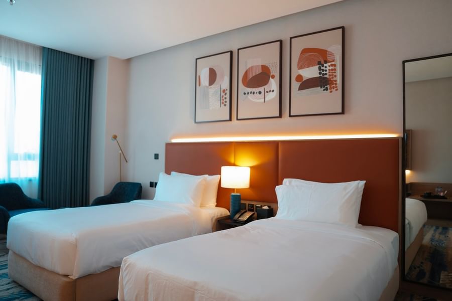 Two twin beds with headboard lighting and artwork above them in a hotel room at Warwick Hotel & Spa Jeddah.