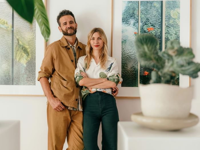 Stylish couple standing together in a bright room adorned with framed botanical art and a potted plant at Hotel Motto Vienna