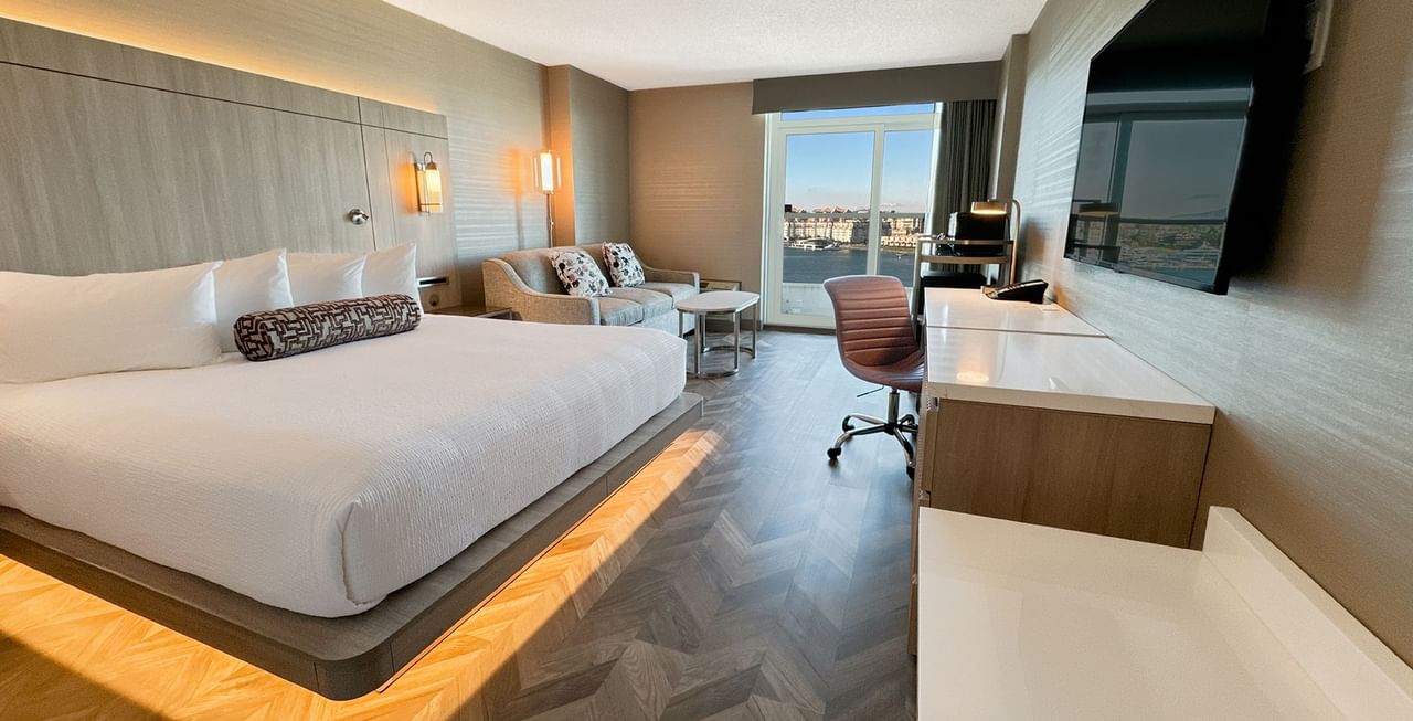 Hotel guestroom with king bed, TV, work desk, chair, couch, and an ocean view.