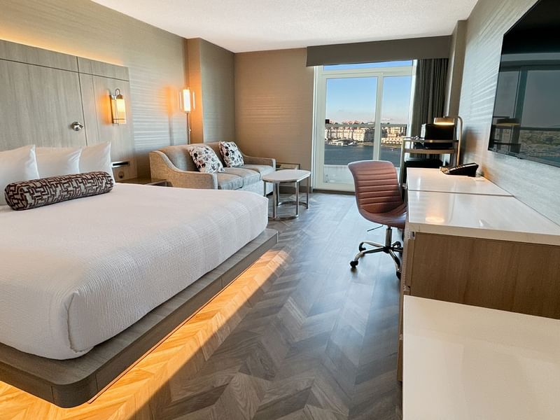 Hotel guestroom with king bed, TV, work desk, chair, couch, and an ocean view.