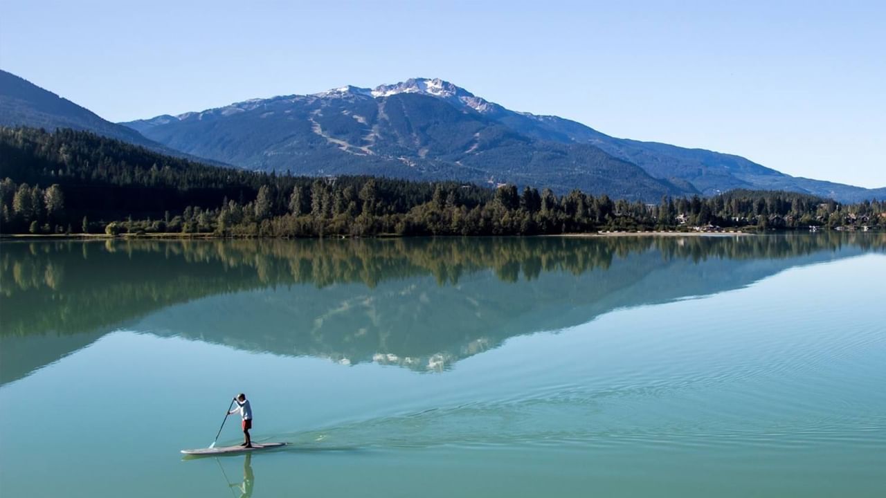 A person paddleboarding on a serene lake with mountain and forest scenery in the background.