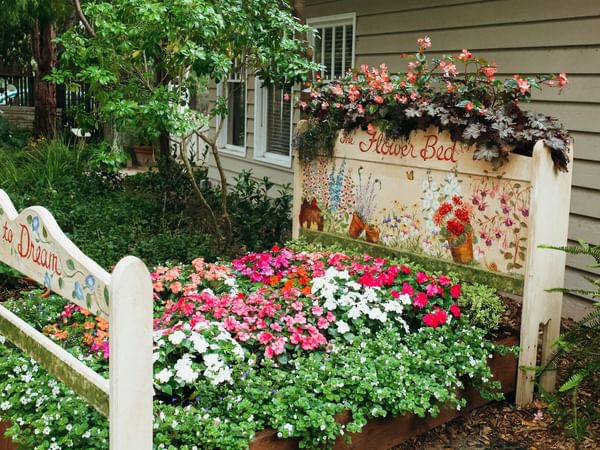 A repurposed bed frame is transformed into a vibrant flower bed in a lush garden.
