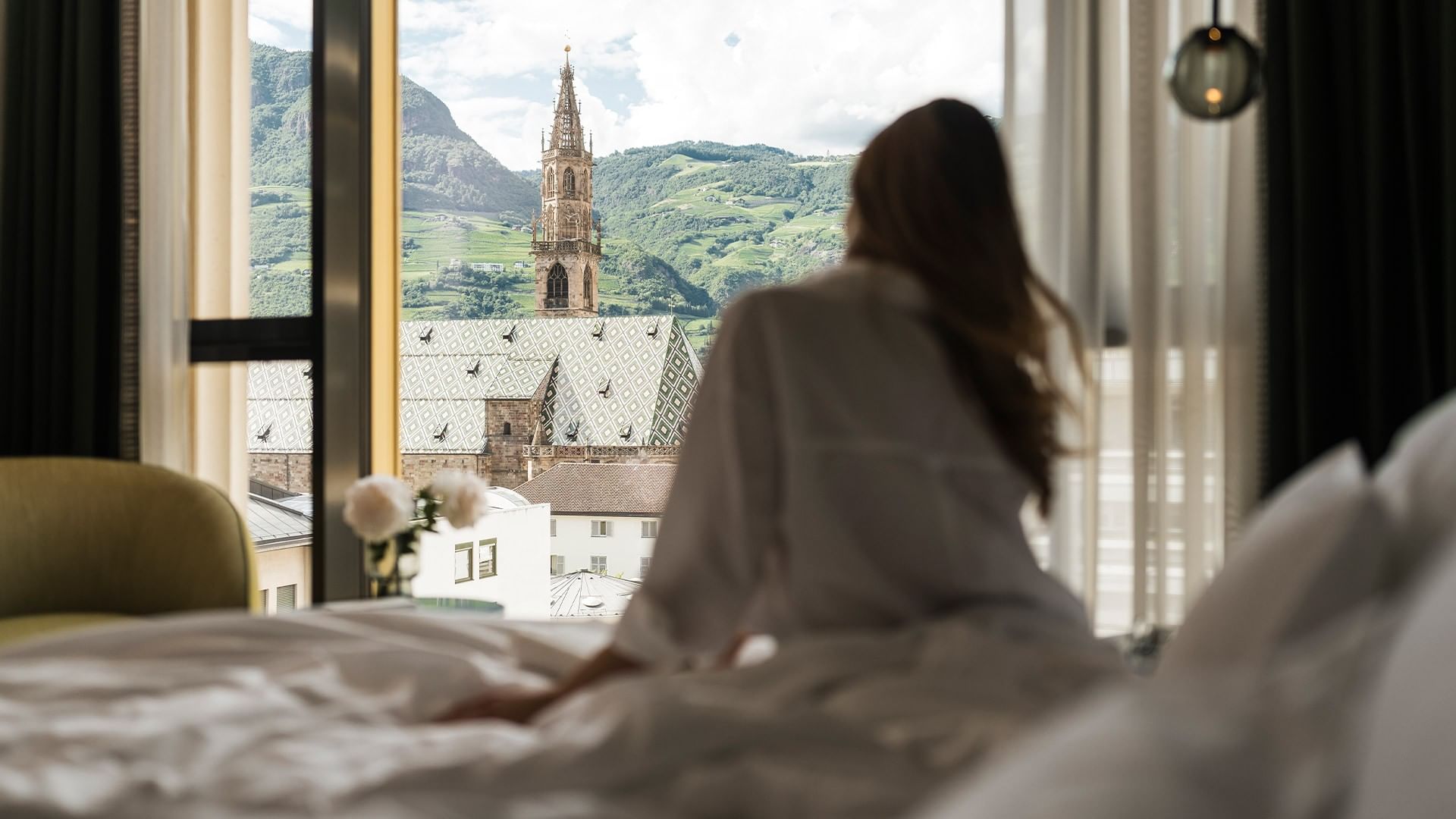 Frau genießt Ausblick auf eine Kirche aus dem Hotelzimmer bei Falkensteiner Hotel Bozen