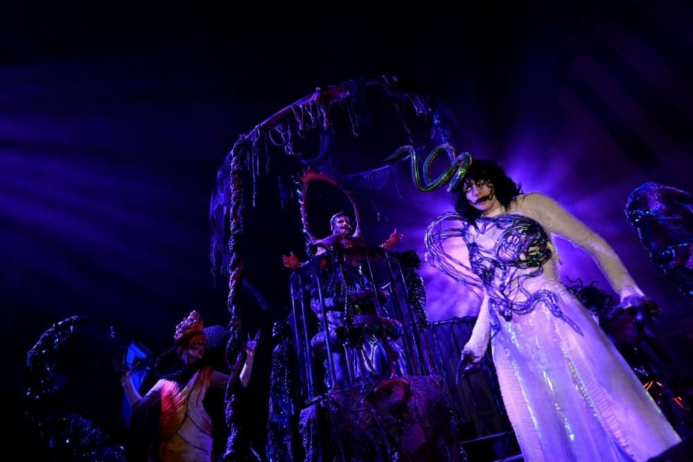 A zombie prom queen looms in purple light with a creepy set behind her.