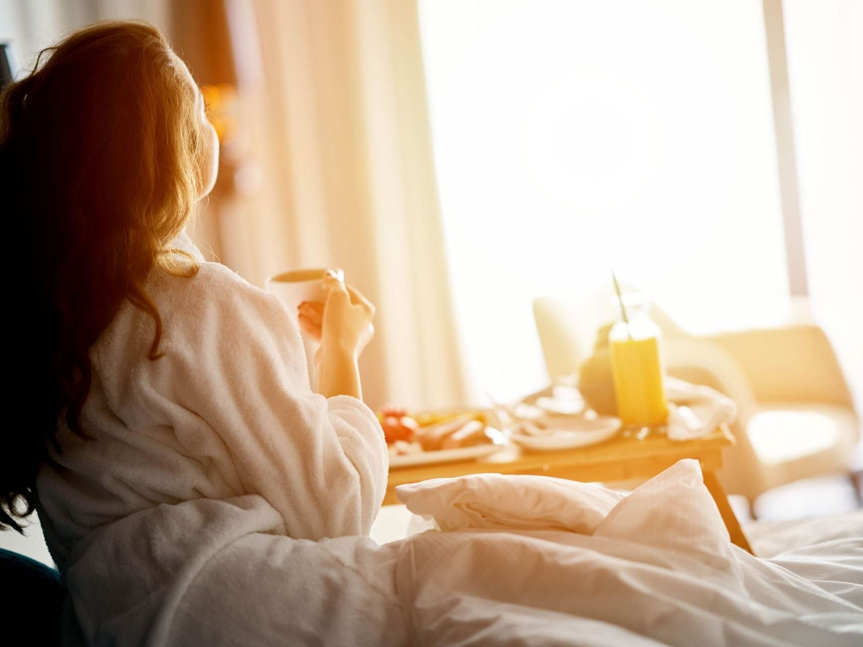 A woman enjoying breakfast in bed at James Cook Hotel Grand Chancellor 