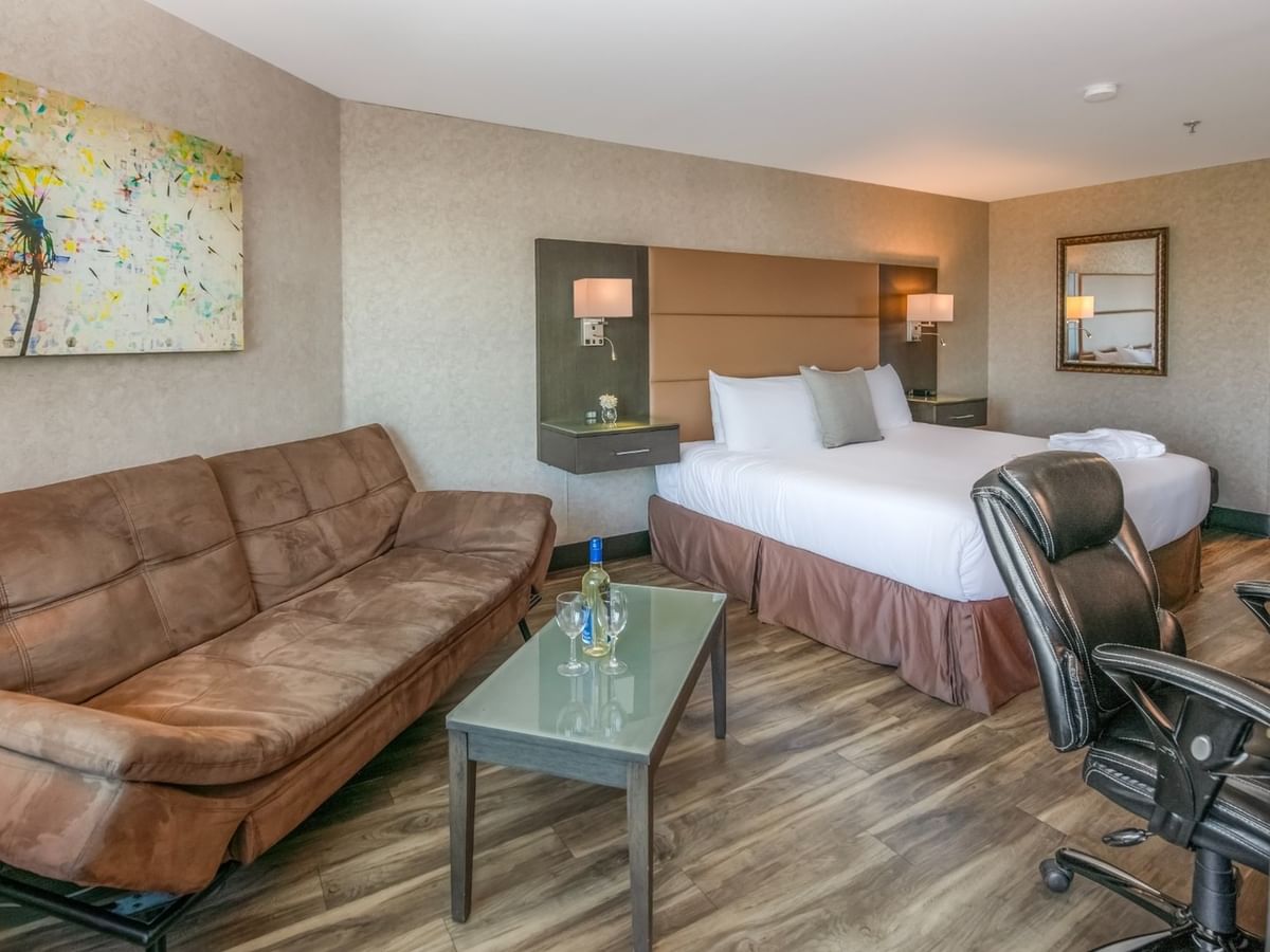 Coast Premium King with Patio with a bed, couch, desk, chair, artwork, and wooden floors at Coast Lonsdale Quay Hotel