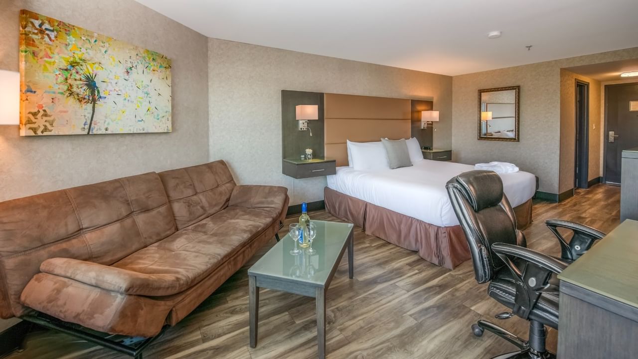 Coast Premium King with Patio with a bed, couch, desk, chair, artwork, and wooden floors at Coast Lonsdale Quay Hotel