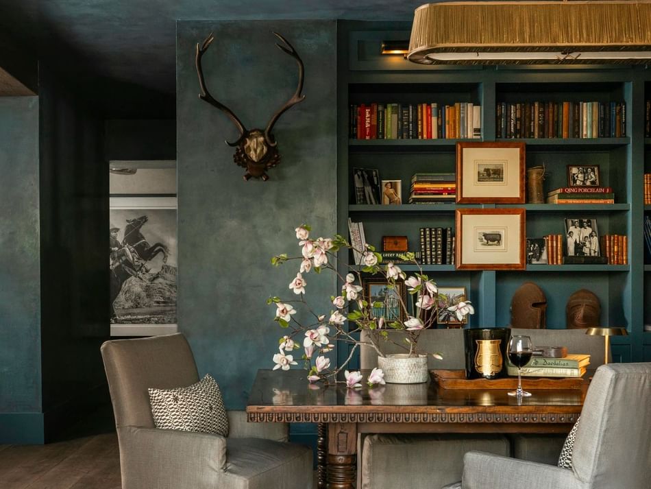The Granduca Library nook at Granduca Houston with a wooden table, armchairs, book-filled shelves, and floral décor