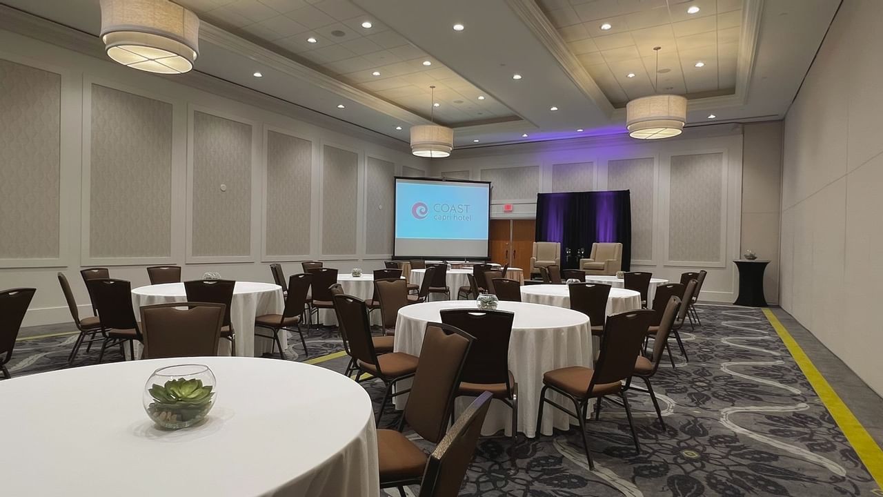 Ballroom with round tables, chairs, stage, podium and presentation screen