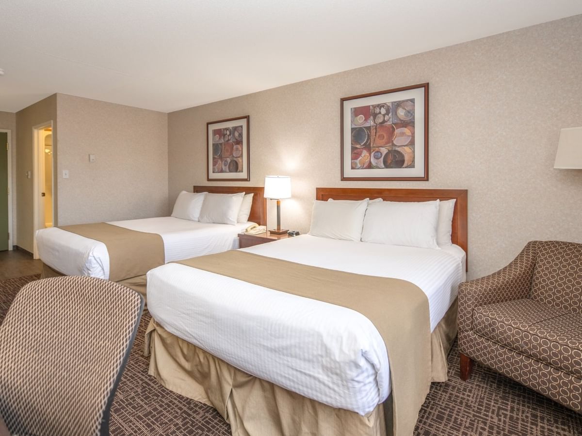 Hotel room with two beds, chairs, nightstands, lamps, and framed artwork on the wall.