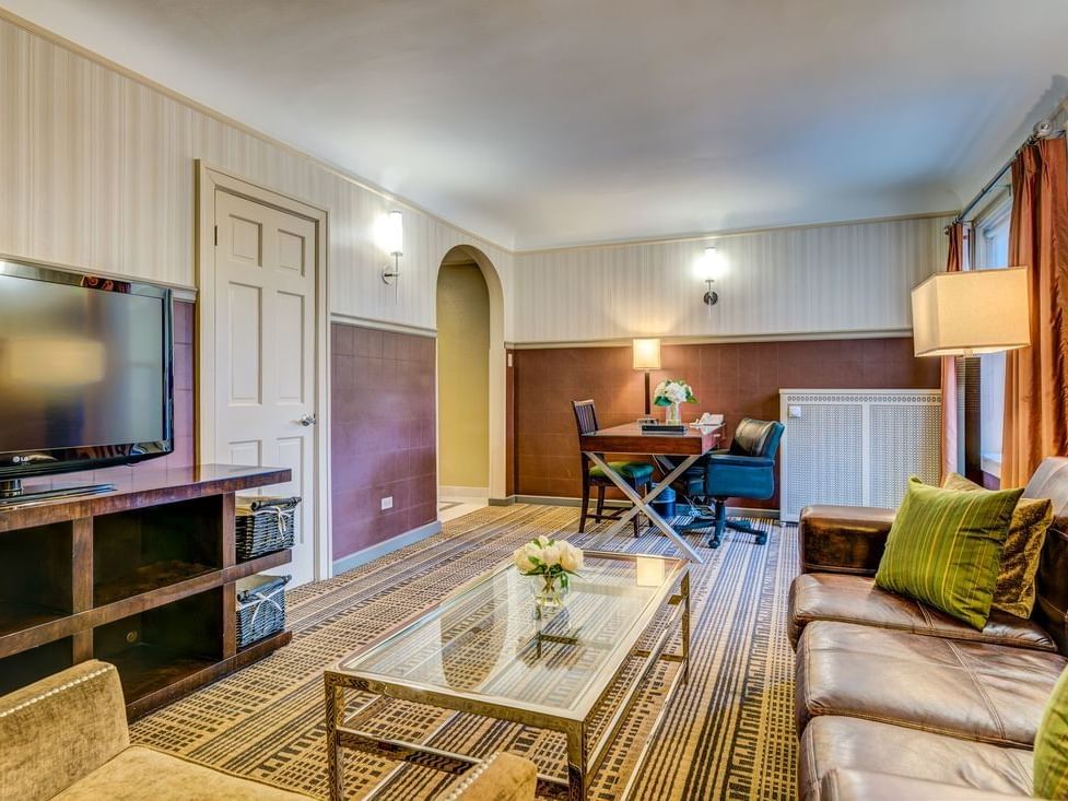 Cozy Suite with TV, leather sofa with green pillows, and a dining table at The Carleton of Oak Park Hotel
