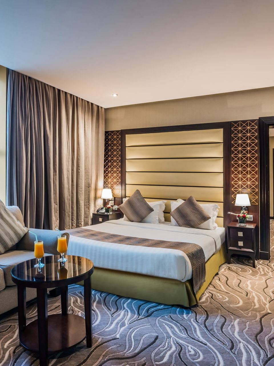 Gray sofa and round table by a striped bed under a padded headboard in Executive Suite at Naviti by Warwick Al Khobar