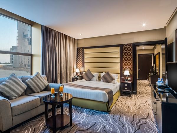 Executive suite with a bed with a sofa facing the TV at Warwick Al Khobar