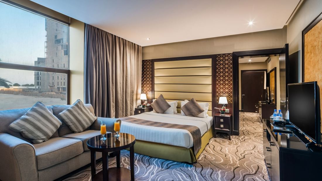 Gray sofa and round table by a striped bed under a padded headboard in Executive Suite at Naviti by Warwick Al Khobar