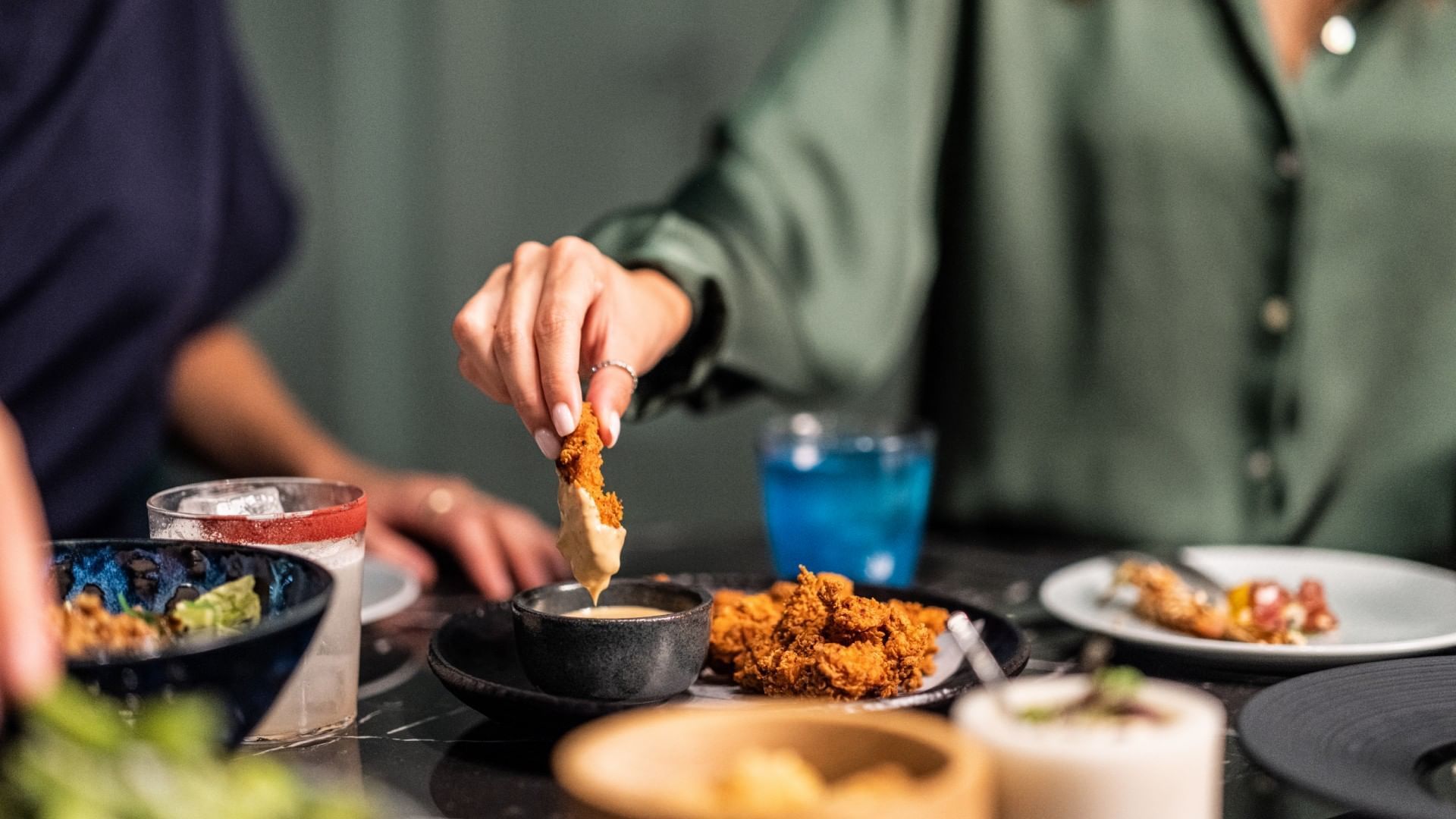 Person dipping fried chicken into sauce in The Monkey Bar at Falkensteiner Hotel Prague