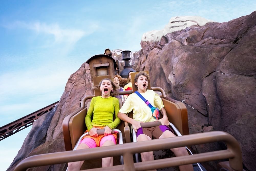 Passengers in a roller coaster seat hold onto their belts and scream while descending a hill surrounded by large rocky walls.  