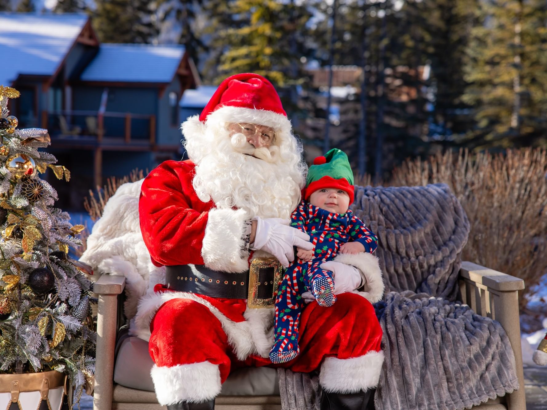 Santa Claus holding a baby in a festive elf outfit near the snowy outdoor cabins at Spring Creek Resorts