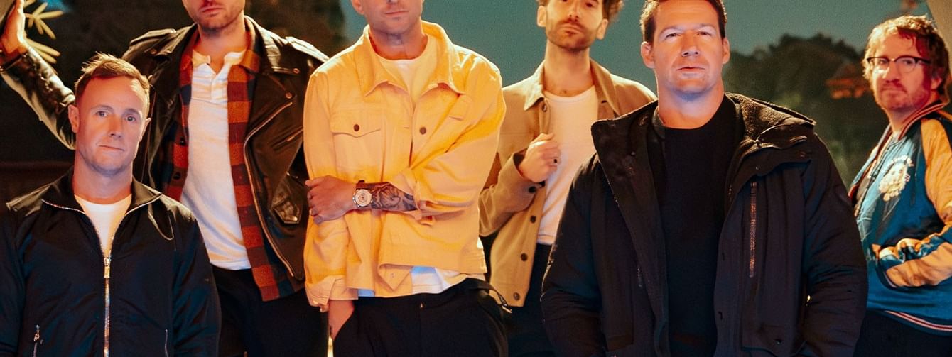 OnRepublic stand on steps under an arch with a patterned frame and blue sky background.