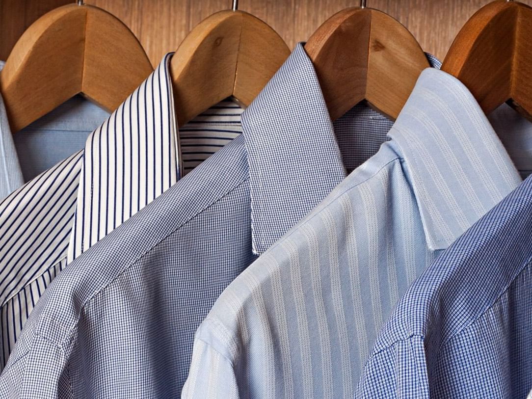 A selection of crisp, blue patterned dress shirts hangs neatly on wooden hangers in a closet at Paramount Hotel Portland