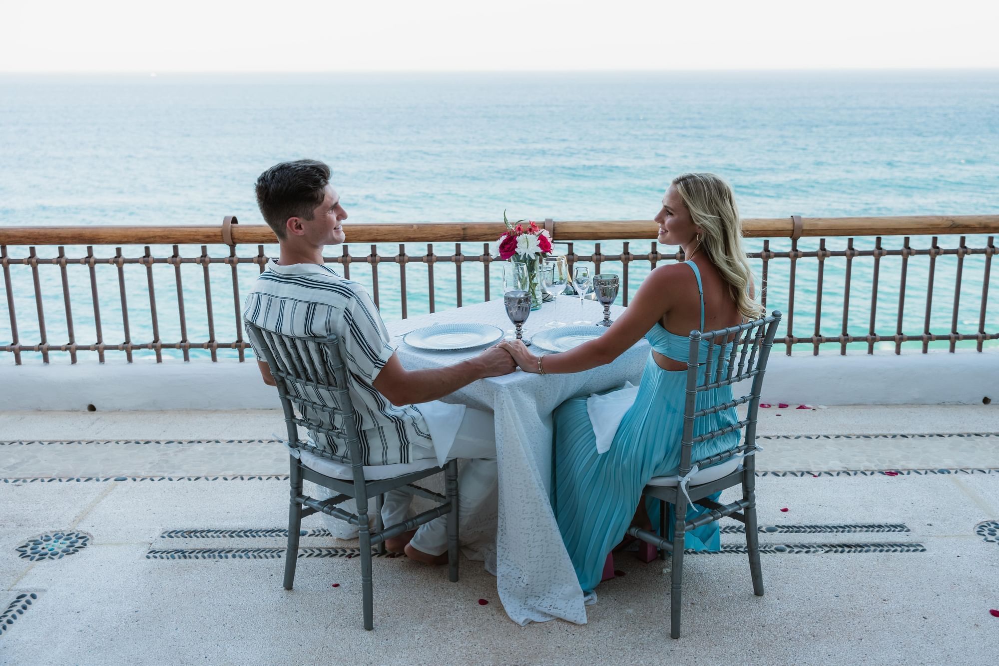 Couple holding hands at a romantic seaside dining table in Marquis Los Cabos