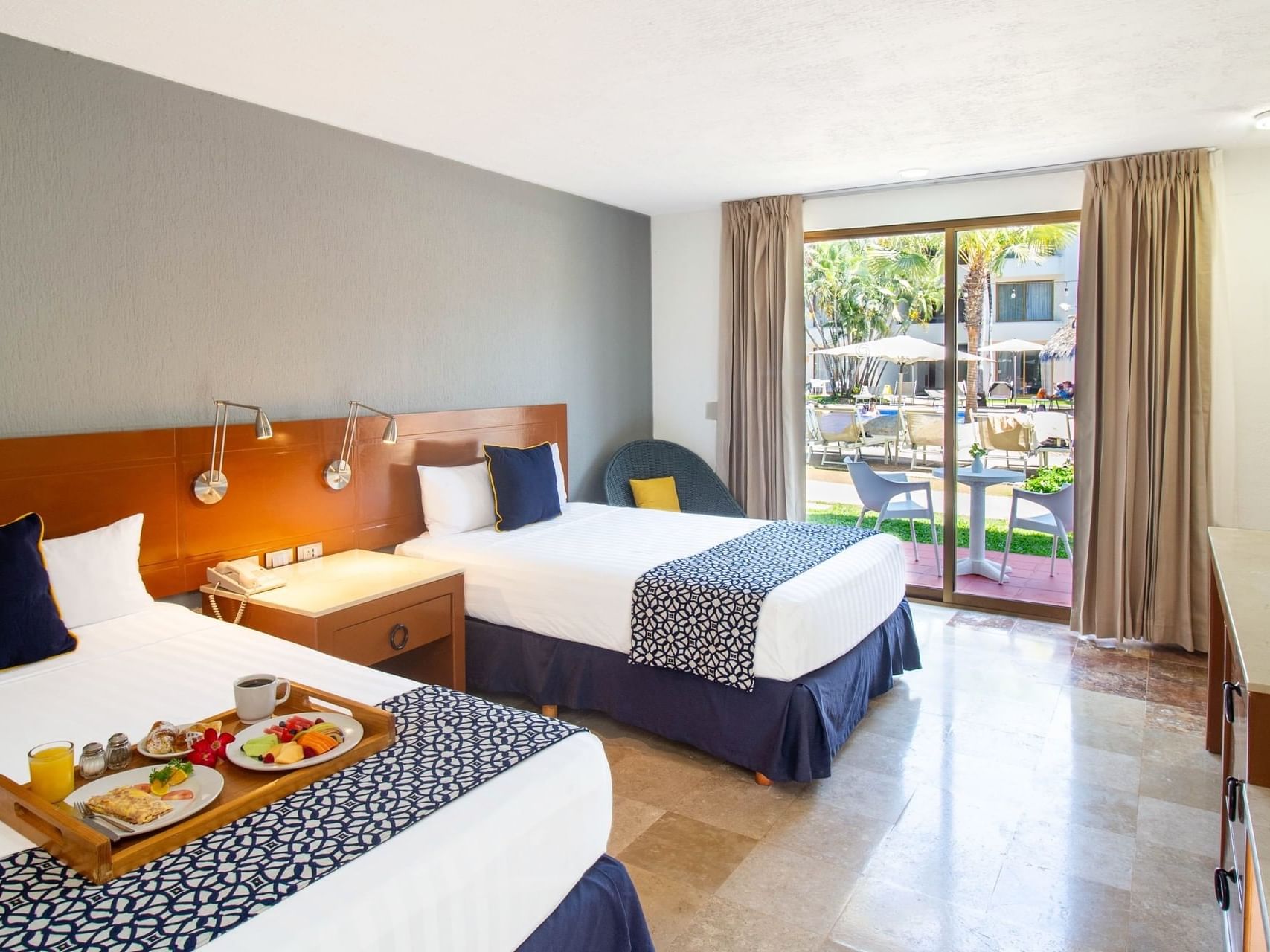 Suite con dos camas con desayuno en una bandeja, y un patio con vista a la piscina, en Guadalajara Plaza Hoteles & Suites